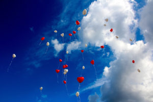 Red and white heart balloons fly high into the sky.