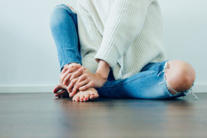 A woman sits on the floor. She holds onto her foot.