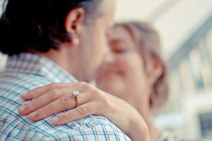 A woman hugs a man. She is wearing a wedding ring and appears happy.