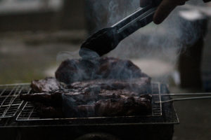 A pair of tongs flips over a piece of steak on a grill.