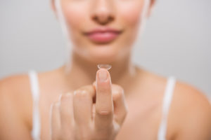 A woman holds a contact lense on her pointer finger.