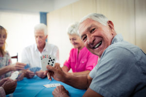 A group of elderly people sit at a table playing cards.