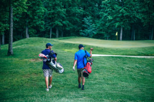Two men walk on a golf course with golf bags.
