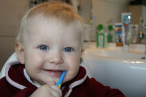 A little boy brushes his teeth with a blue toothbrush.