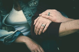 Two people lock their arms together. They both wear wedding rings.