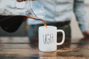 A person pours coffee into a coffee mug that says, "UGH."