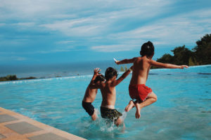 Three young boys, wearing swimsuits, jump into a lake.