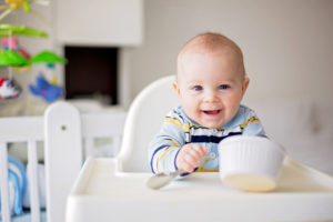 A baby sits at a feeding chair and smiles.