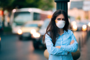 A woman wears a medical mask outside and crosses her arms.