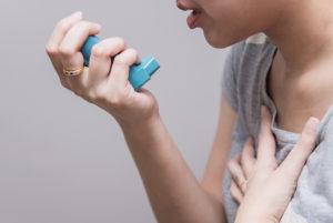 A woman appears to be using her asthma inhaler.