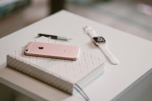 A journal sits on a bedside table next to an iPhone, pen and Apple Watch.