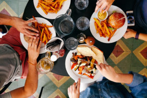 Four people gather at a table to eat hamburgers and pasta.