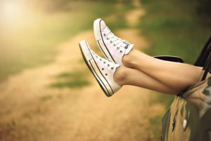 A woman wearing Converse sneakers puts her feet out the window of a moving car. 