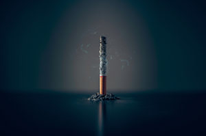 A cigarette, sitting on its ashes, is in focus.