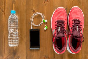 Tennis shoes, a phone with earbuds attached and a water bottle is in focus.