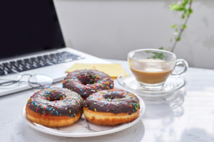 Three sprinkled donuts are plated next to a cup of coffee and a laptop.