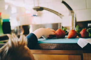 A kid reaches for strawberry.