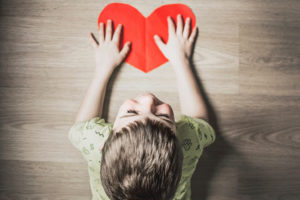 A young boy puts his hands on a red heart-shaped piece of paper.