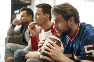 A man holds a football and watches TV with two men.
