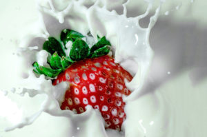 A strawberry falls into a glass of milk.