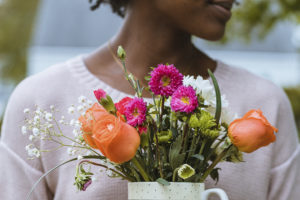 A woman holds a mug full of flowers.
