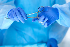 Surgical scissors are passed by one person in medical gloves to another.