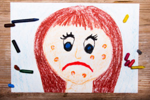 A drawing of a girl frowning with blemishes on her face.