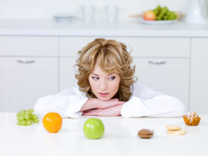A woman looks at a counter with fruit and bakery items. Her eyes are staring directly at a cookie.