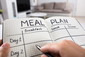 A person writes in a journal their meal plans for breakfast, lunch and dinner.