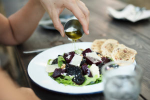 A person pours olive oil onto a salad.
