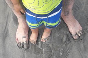 A kid stands in wet sand with an adult.