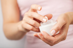A woman dips her finger into a bottle full of skin cream.