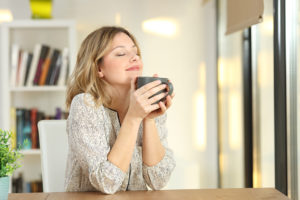 A woman holds a coffee mug close to her face, closes her eyes and smiles.