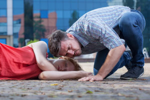 A man appears to be listening to a woman's breathing as she lies on the ground.