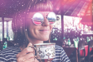 A woman in sunglasses holds a cup of coffee.