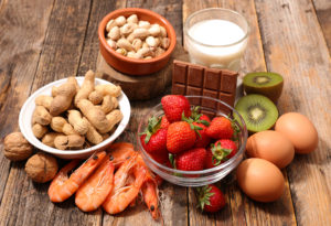 Strawberries, kiwi, eggs, peanuts, walnuts, chocolate, shrimp and milk are in focus.