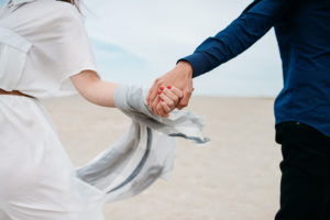A man and woman hold hands at the beach.