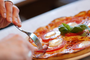 A person cuts into their pizza with a fork and knife.