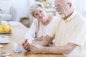 An elderly man looks at a pill bottle. An elderly woman looks on.