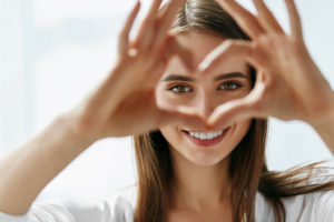A woman shapes her fingers to create a heart. Her eyes are in focus.