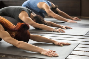 Three women participate in yoga, stretching on a yoga mat.