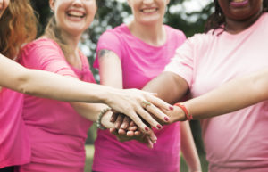 Five women in pink T-shirts put their hands together and smile.