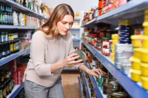 A woman grabs a canned food from a grocery aisle.