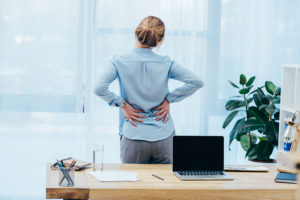 A person stands up from her desk and stretches her back. 