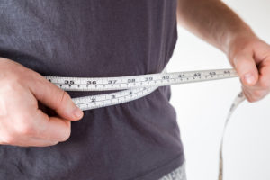 A person measures their waist with measuring tape.