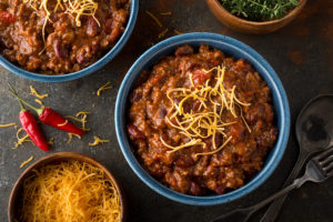 Turkey chili is in focus with cheese on top.