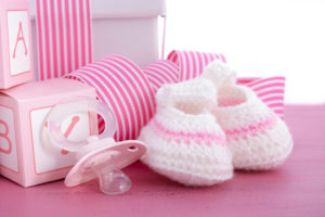 Pink baby blocks, pink ribbon, pink knitted baby shoes, and a pink pacifier are in focus.