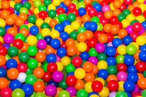 Colorful plastic balls from a ball pit are in focus. The colors range from blue, green, yellow, orange, red, pink and white.