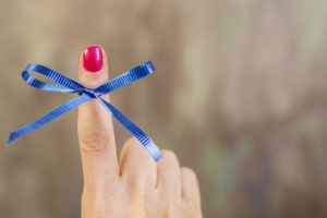 Blue social awareness ribbon tied in a bow around a woman's index finger. The blue ribbon represents various causes including colon cancer. 