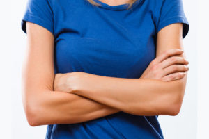 A woman crosses her arms and appears frustrated. She is wearing a blue T-shirt.